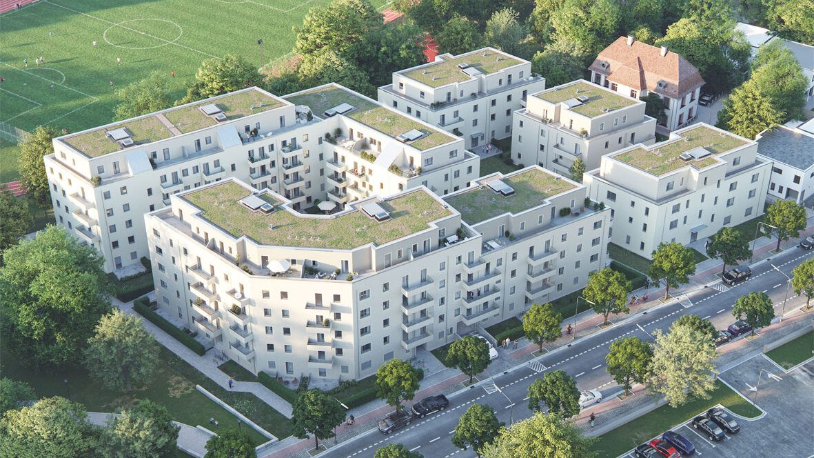 Luftperspektive eines mehrteiligen Wohnensembles mit begrünten Dächern und Innenhof. Das Quartier liegt an einer Straße mit Baumbestand, angrenzend an Sportflächen.