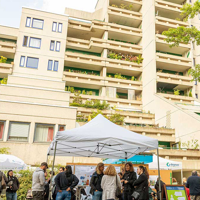 Gruppenaufnahme während der Informationsveranstaltung zur Sanierung der Schöneberger Terrassen. Mitarbeiter von degewo stehen mit Mieterinnen und Mietern vor dem Gebäude zusammen und reden.
