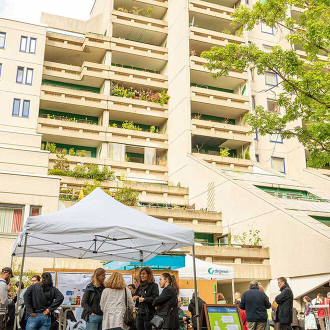 Gruppenaufnahme während der Informationsveranstaltung zur Sanierung der Schöneberger Terrassen. Mitarbeiter von degewo stehen mit Mieterinnen und Mietern vor dem Gebäude zusammen und reden.