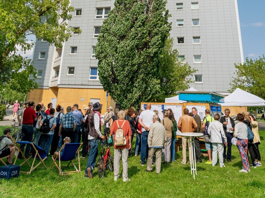 Zahlreiche Anwohnende versammeln sich vor einem degewo-Hochhaus zur Beteiligungsveranstaltung und diskutieren die Planungen.