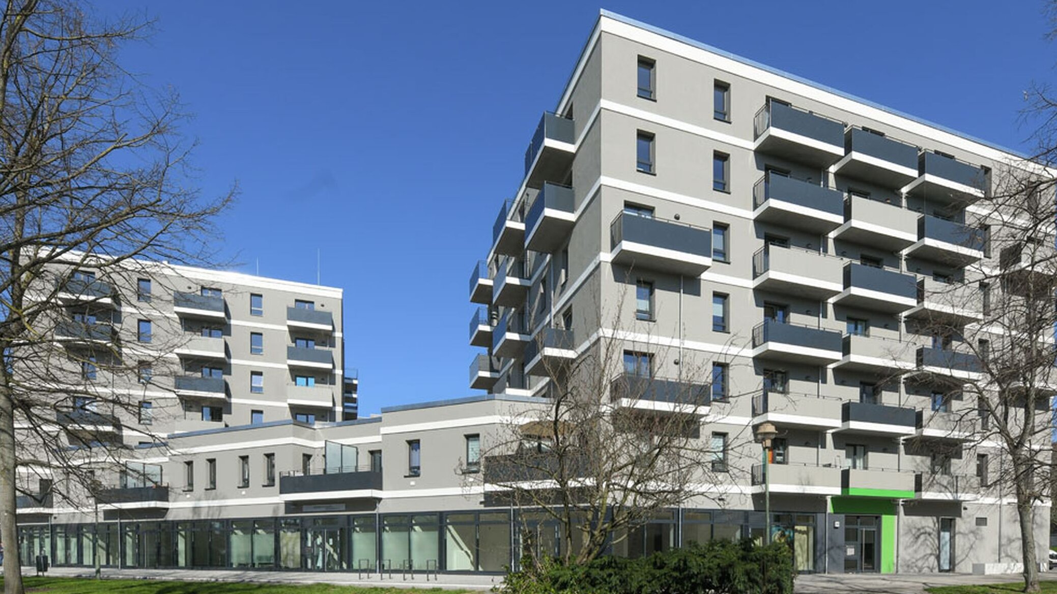 Außenansicht degewo-Neubau Mehrower Allee 28 und 30 mit Rasenflächen, Wegen und Bäumen im Vordergrund.