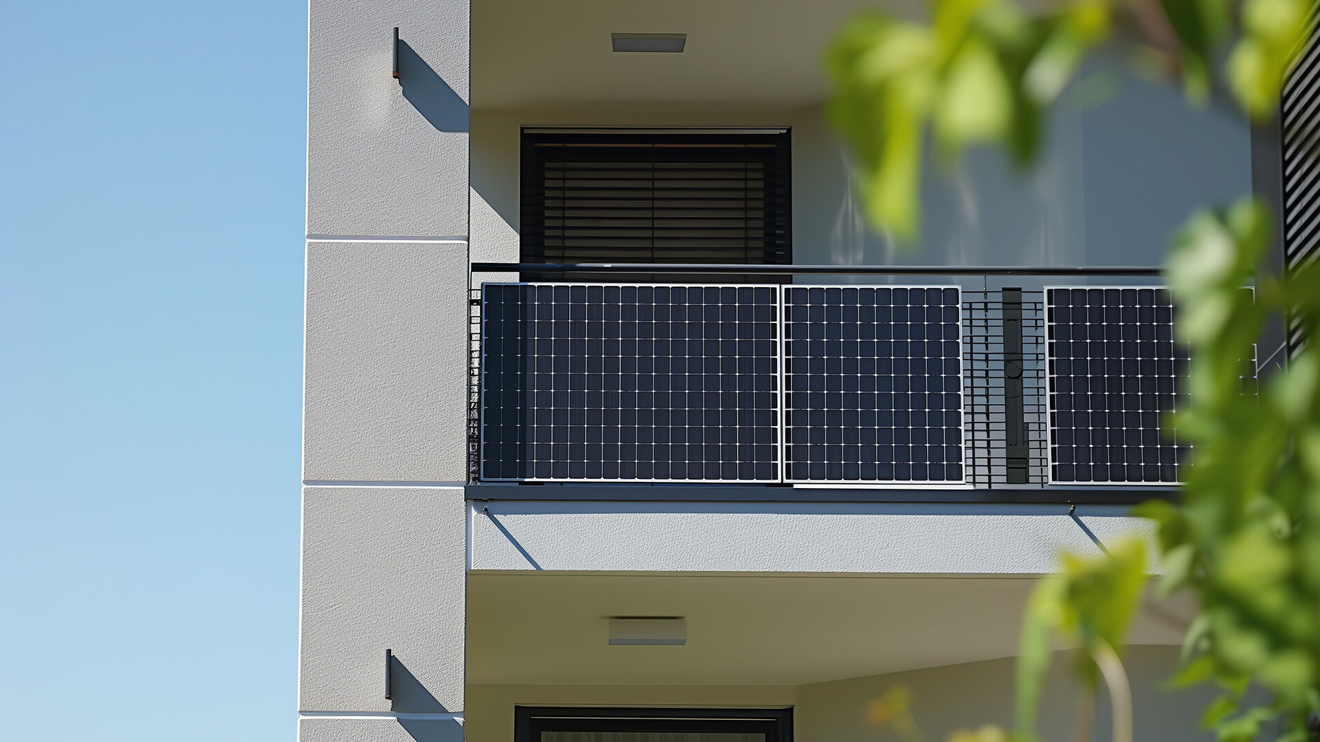 Balkon eines Mehrfamilienhauses mit installiertem Balkonkraftwerk. Die Solarmodule sind am Geländer befestigt, im Hintergrund ist die Fassade des Gebäudes und blauer Himmel zu sehen.