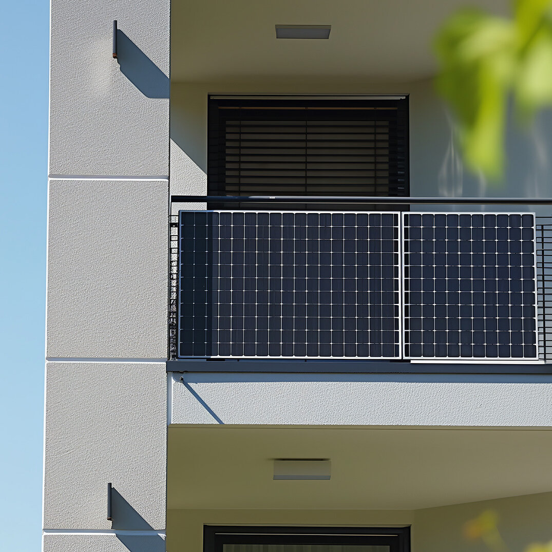 Balkon eines Mehrfamilienhauses mit installiertem Balkonkraftwerk. Die Solarmodule sind am Geländer befestigt, im Hintergrund ist die Fassade des Gebäudes und blauer Himmel zu sehen.