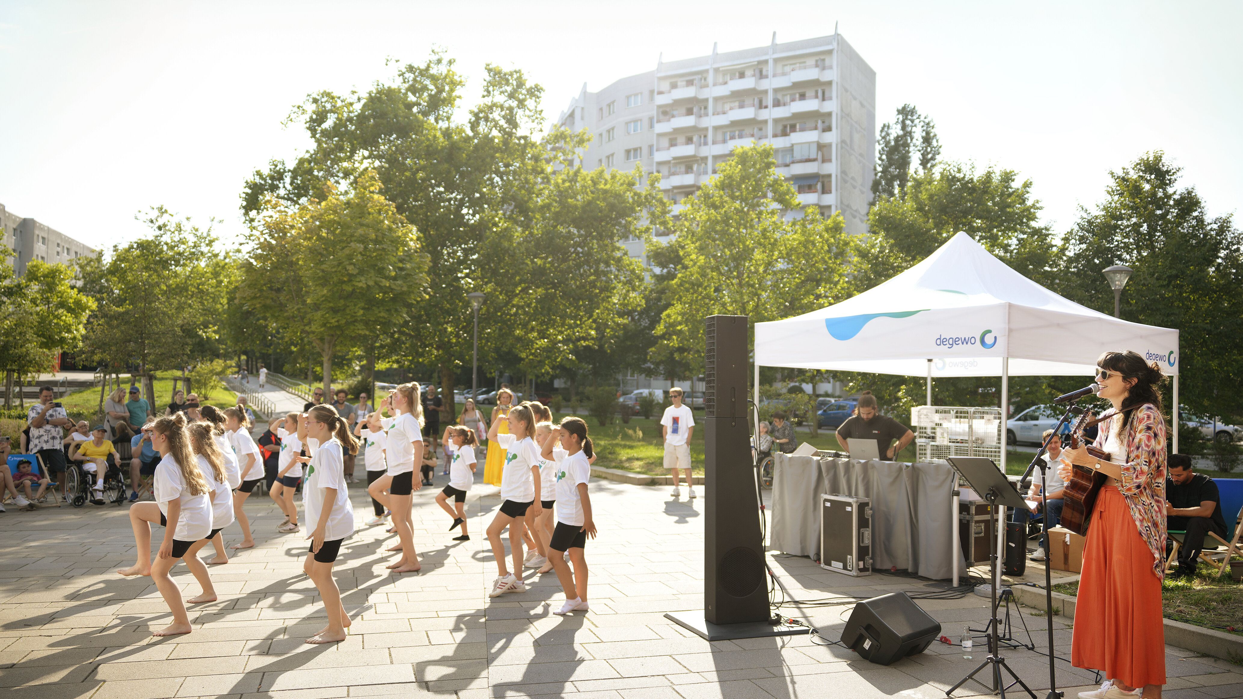Kinder tanzen vor Bühne, Musikerin singt unter Pavillon.