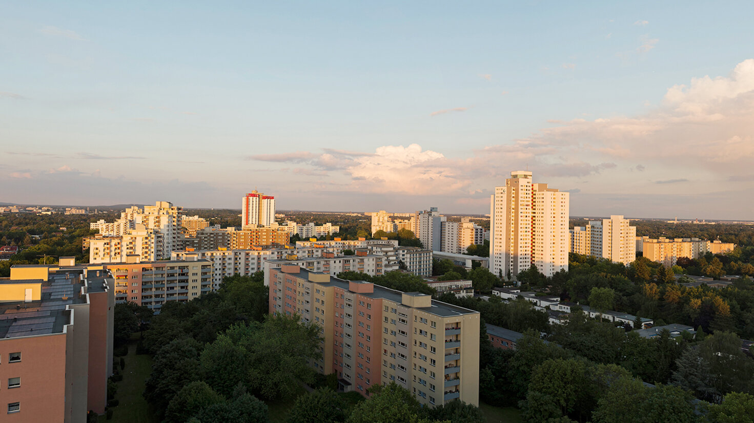 Weitläufiger Blick über die Gropiusstadt mit zahlreichen Wohnhochhäusern, niedrigeren Wohnbauten und großen Grünflächen im warmen Licht der Abendsonne.