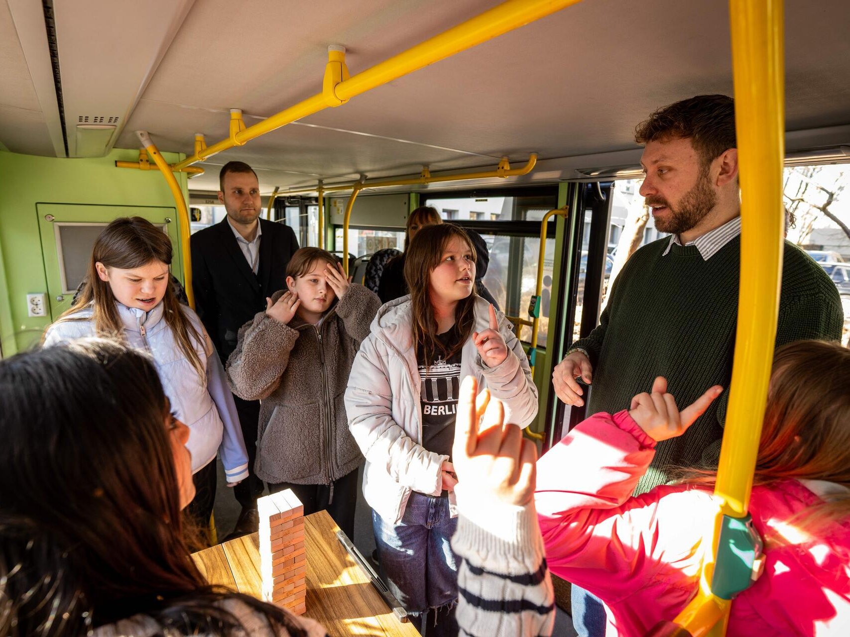 Eine Gruppe Kinder und zwei Erwachsene stehen im Demokratie-Mobil und spielt Demokratie-Jenga. Zwei der Kinder melden sich.