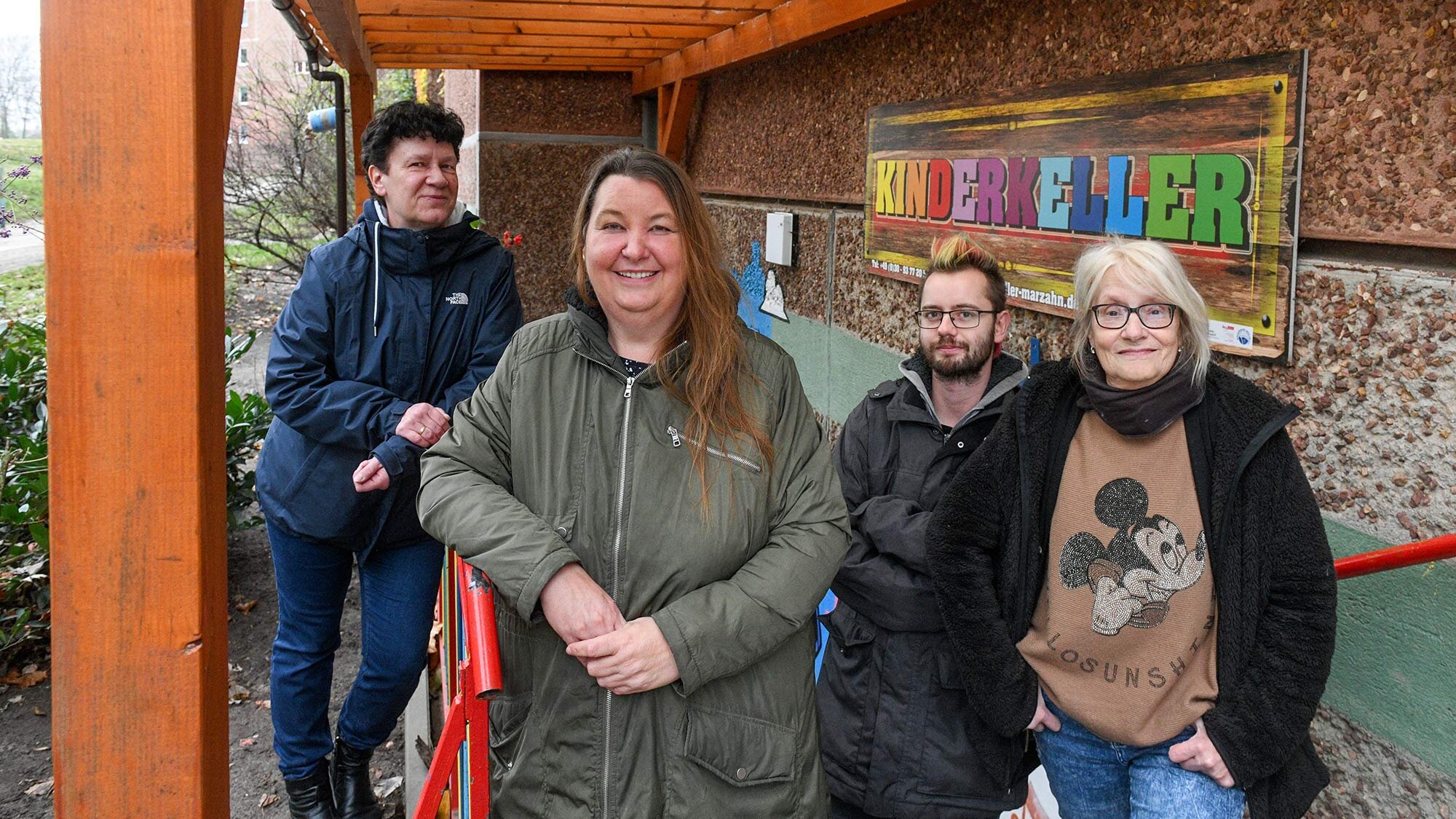 Vier Personen stehen vor dem Eingang des „Kinderkellers“ unter einem Holzvordach. Alle lächeln in die Kamera.