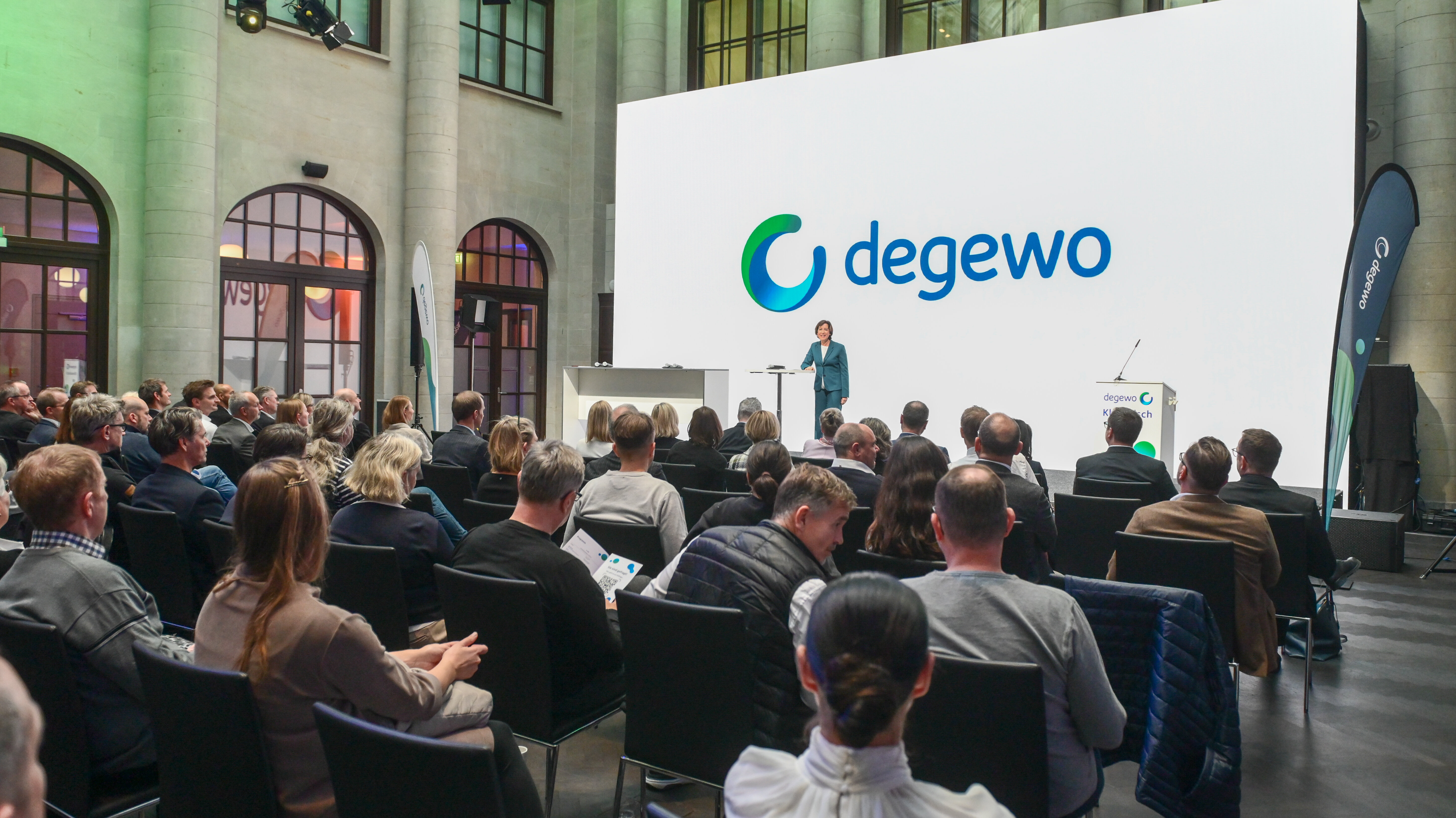 Vortrag auf Bühne vor Publikum mit großer Leinwand und degewo-Logo.