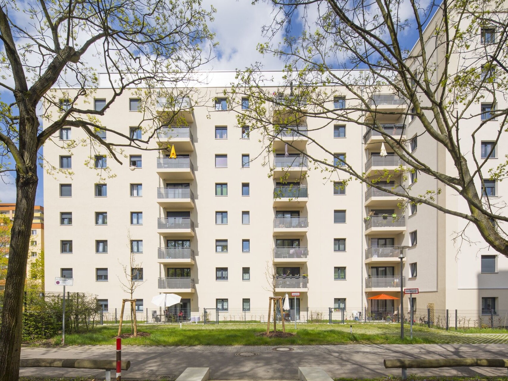 Außenansicht degewo-Neubau Tirschenreuther Straße 8 und 8A: Hofseite mit Baum und Sitzbalken je links und rechts.