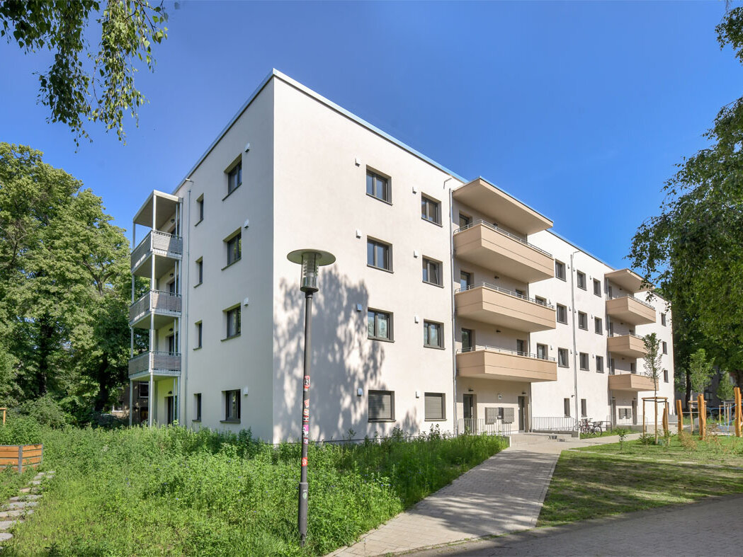 Außenansicht degewo-Neubau Ottomar-Geschke-Straße mit Grünflächen, Wegen und Straßenlaternen im Vordergrund.