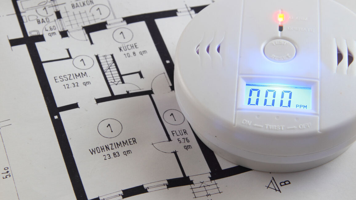 Ein Kohlenmonoxidmelder liegt auf einem Wohnungsgrundriss. Das Display zeigt einen Messwert von 0 und eine kleine Kontrollleuchte ist aktiviert.