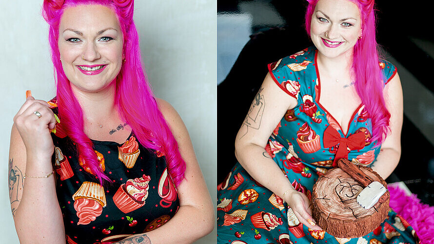 Die Konditorin Franziska Schmidt lächelt in die Kamera. Die Haare sind pink. Sie trägt ein auffälliges Kleid mit Törtchen darauf. Sie hält eine Torte in Form eines Baumstamms inklusive kleiner Axt in den Händen. 