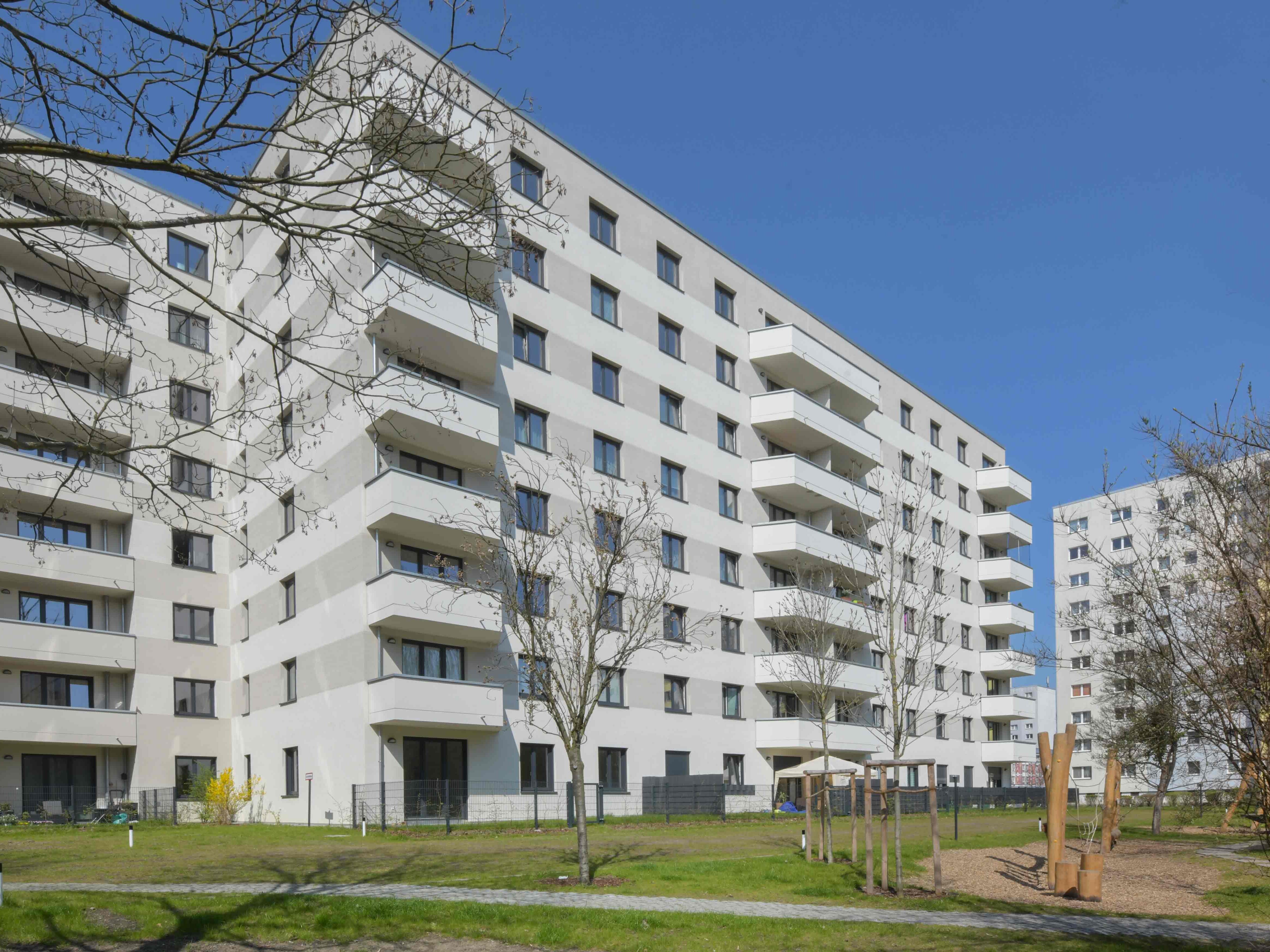 Außenansicht degewo-Neubau Wuhlestraße 2 bis 8 mit Rasenflächen, Bäumen, Weg und Spielplatz im Vordergrund.