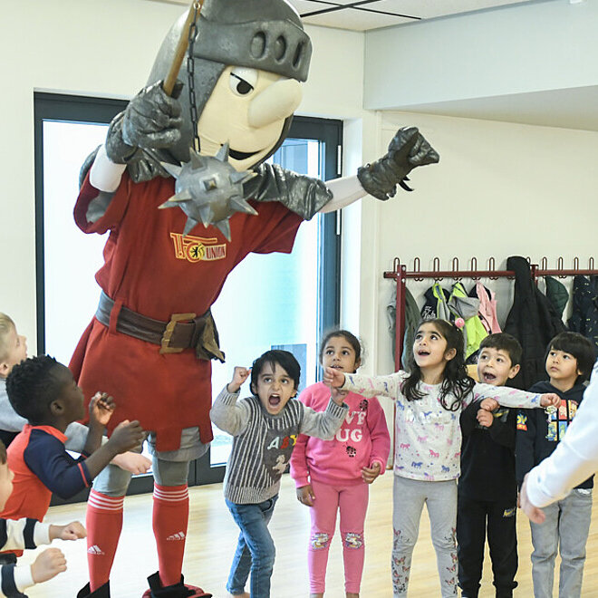 Ein Trainer vor einer Kindergruppe mit Maskottchen