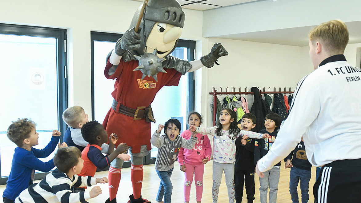 Ein Trainer vor einer Kindergruppe mit Maskottchen