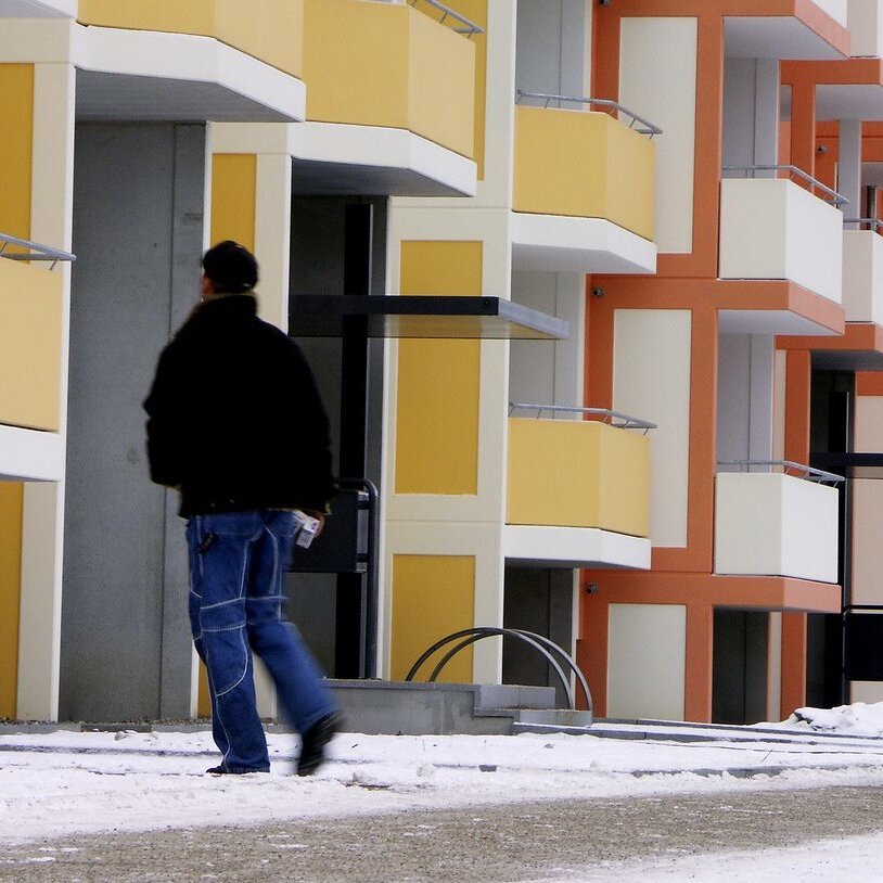 Wohnanlage im Winter mit gestreutem Fußgängerweg. Ein Mitarbeiter läuft den Weg ab.