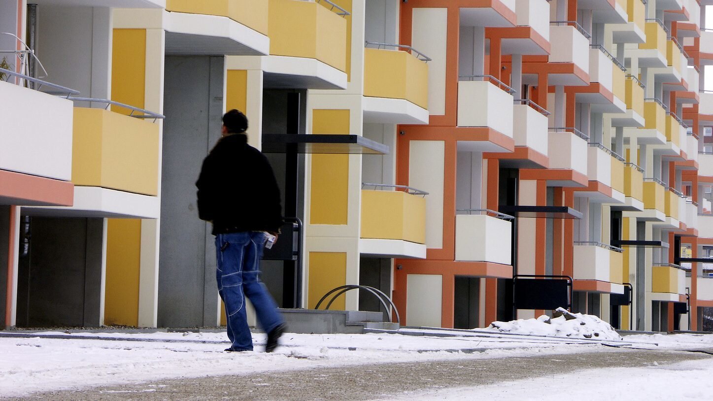 Wohnanlage im Winter mit gestreutem Fußgängerweg. Ein Mitarbeiter läuft den Weg ab.
