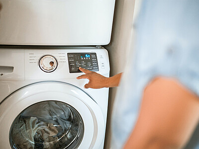 Eine Waschmaschine voller Wäsche wird von einer Person bedient.