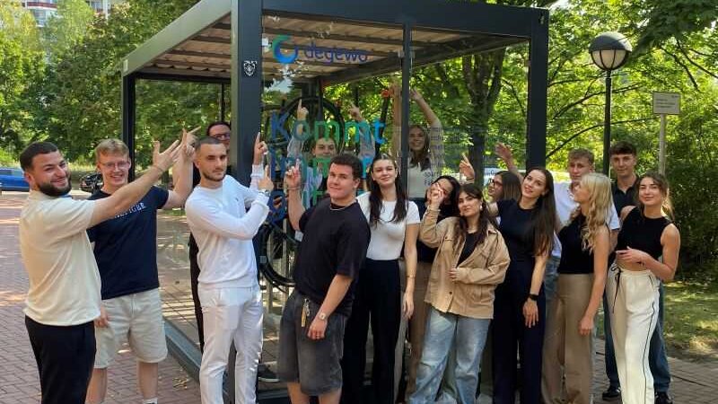 Gruppe junger Menschen steht vor einer überdachten Fahrradstation im Freien und zeigt nach oben