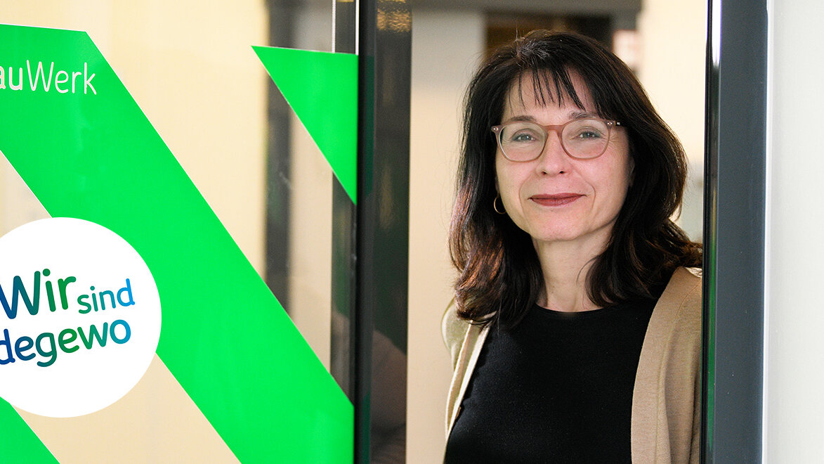 Porträt einer Frau mit Brille vor einer Glaswand mit grünem Schriftzug „Wir sind degewo“, sie blickt freundlich in die Kamera.