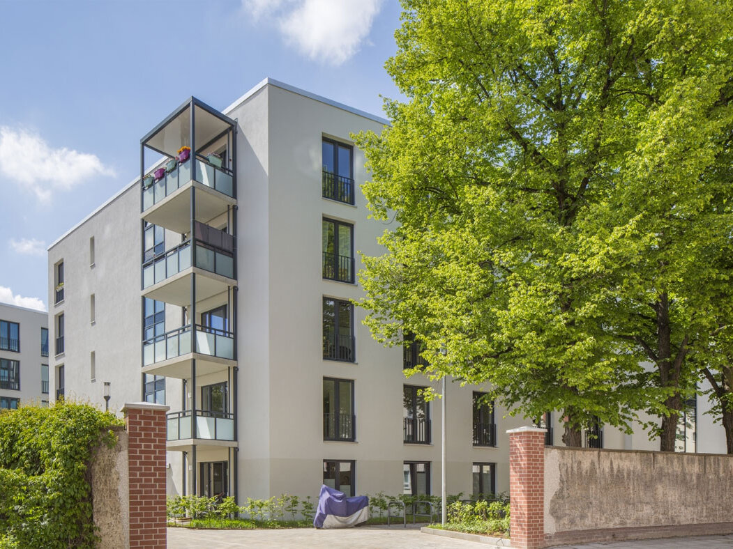 Außenansicht degewo-Neubau Luisenstraße 24 bis 24 A: Auffahrt mit bewachsener Mauer links sowie Mauer und Bäumen dahinter rechts im Vordergrund.