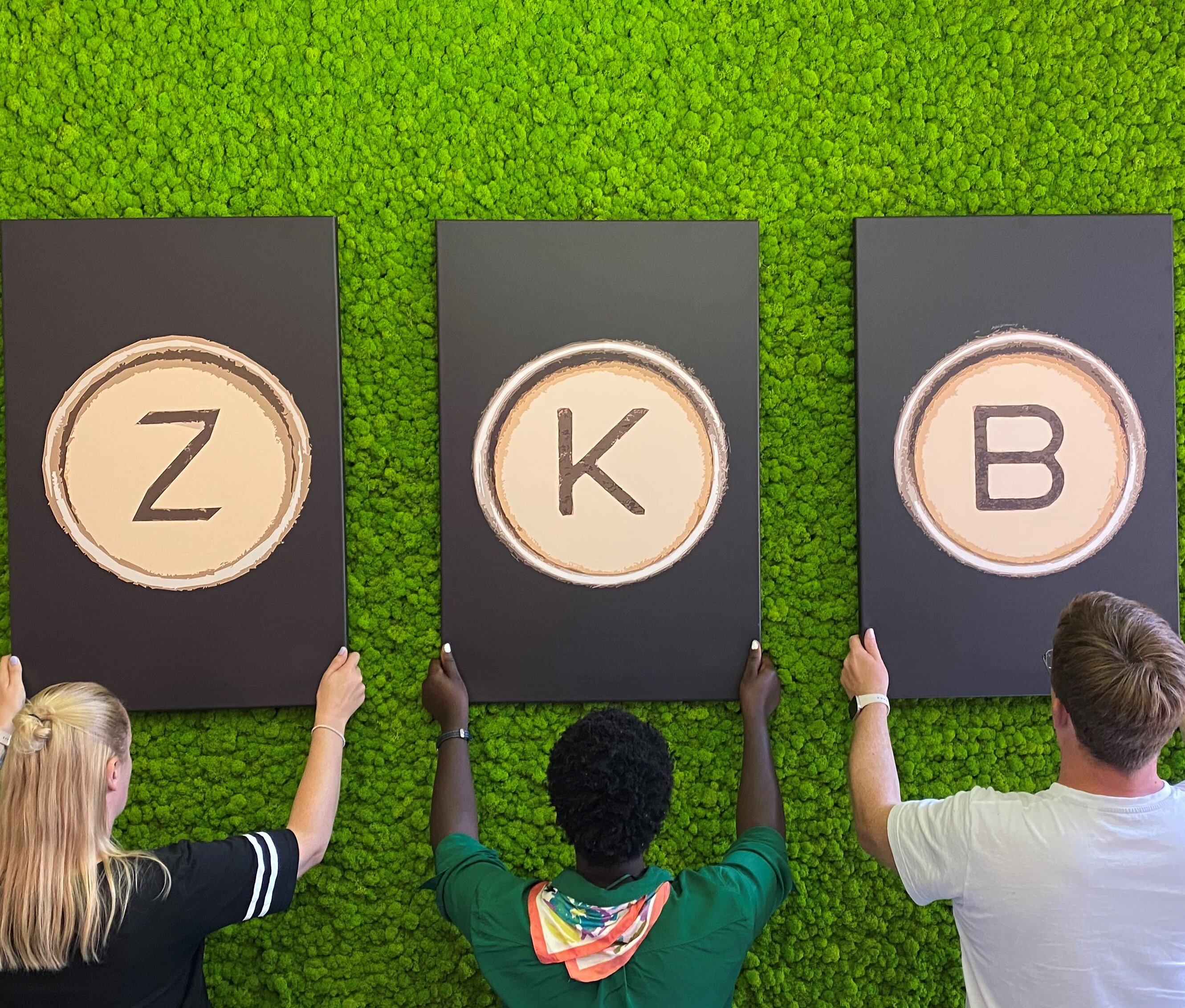 Mitarbeitende der zentralen Kundenberatung hängen die Buchstaben ZKB an eine grüne Wand.