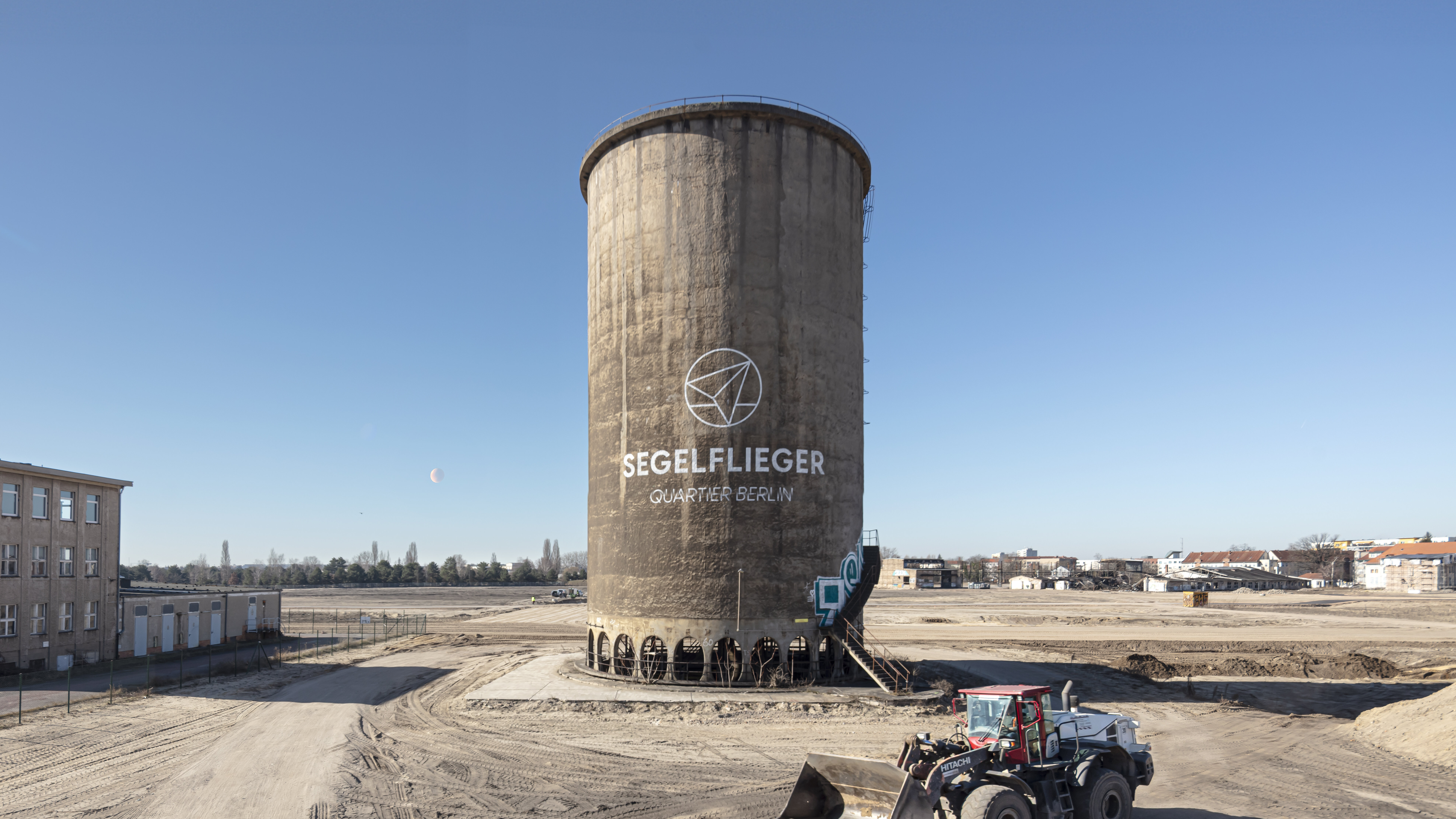 Großer runder Betonturm auf einer Baustelle mit Radlader im Vordergrund.