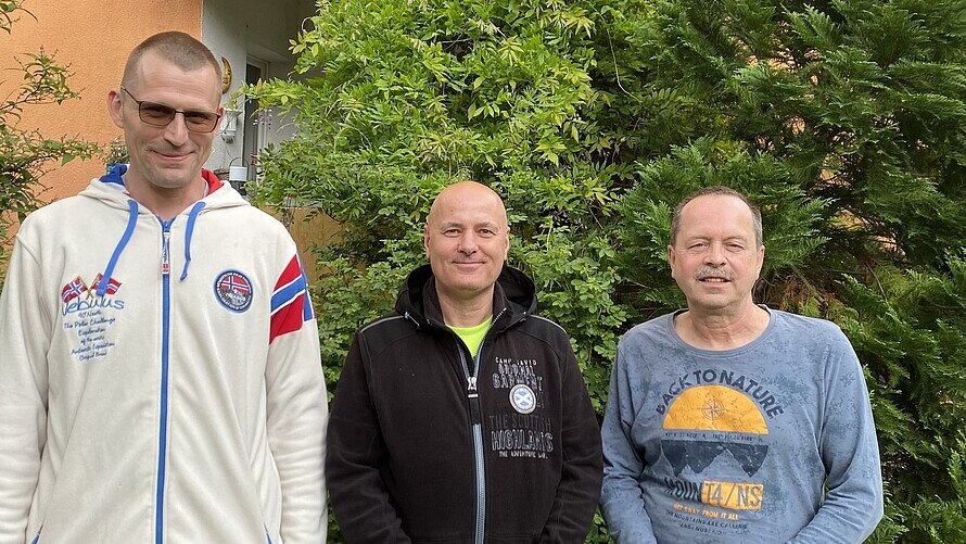Zu sehen sind Sebastian Runge, Mario Kübler und Bernd Schumann von den Beetbrüdern vor einer grünen Hecke in ihrem Garten in der Pechsteinstraße.