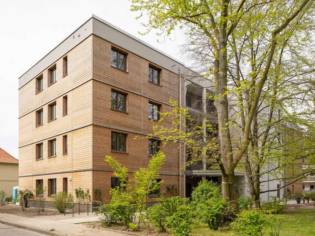 Außenansicht degewo-Neubau Beyrodtstraße 52 mit Weg, Grünfläche, Sträuchern und Bäumen im Vordergrund.