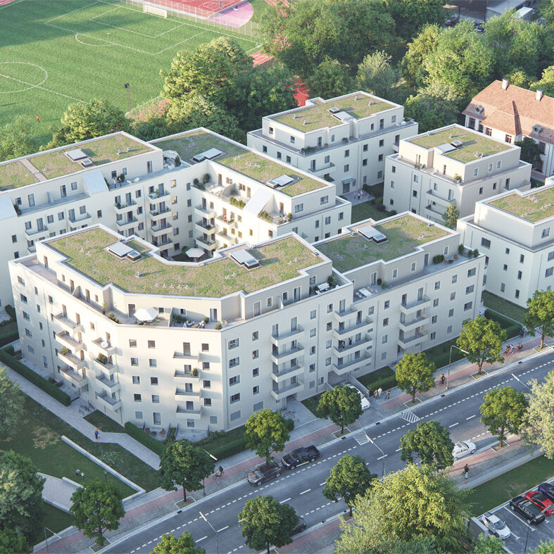 Luftperspektive eines mehrteiligen Wohnensembles mit begrünten Dächern und Innenhof. Das Quartier liegt an einer Straße mit Baumbestand, angrenzend an Sportflächen.