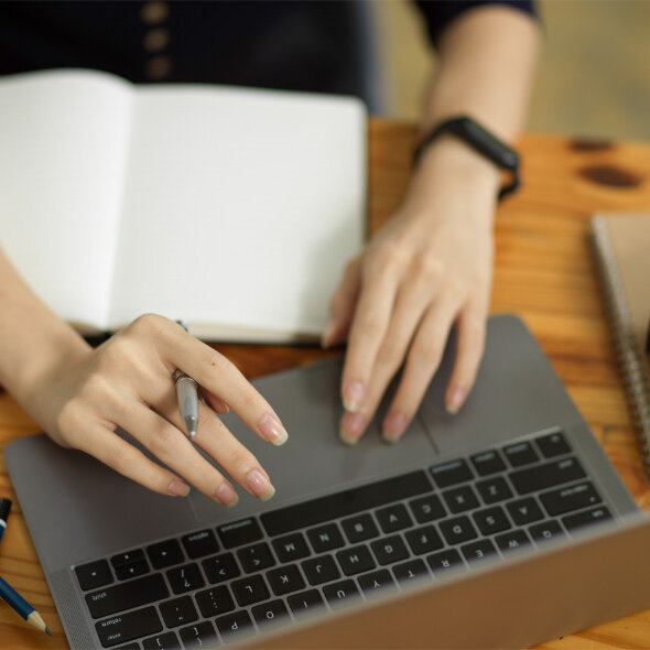 Eine Frau arbeitet am Laptop. Vor ihr liegt ein offenes Notizbuch.