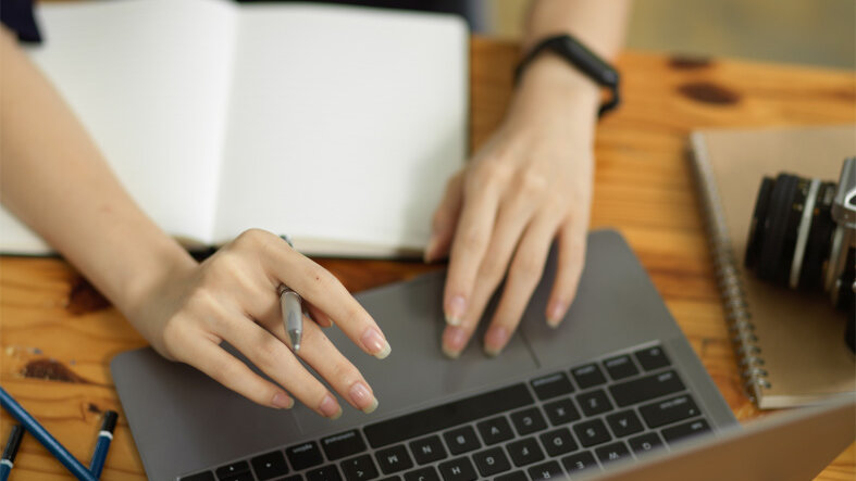 Eine Frau arbeitet am Laptop. Vor ihr liegt ein offenes Notizbuch.