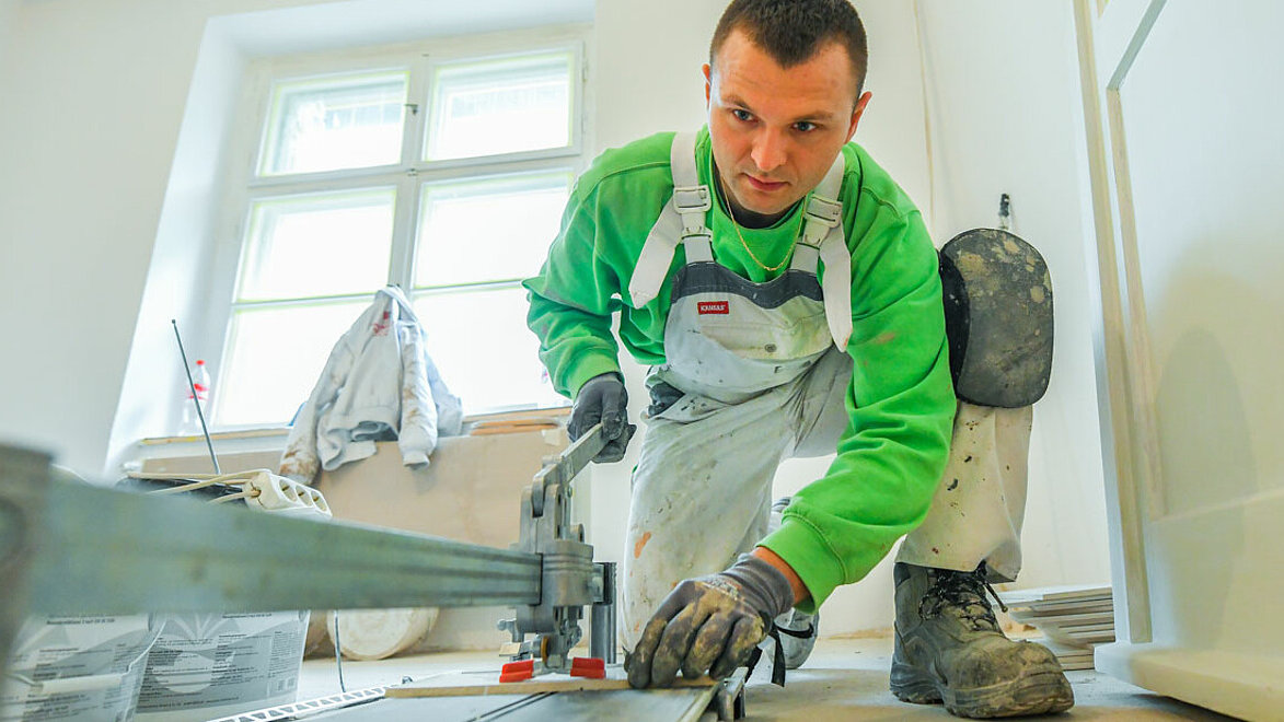 Ein Handwerker der degewo technischen Dienste verarbeitet auf dem Badboden kniend Rigipsplatten