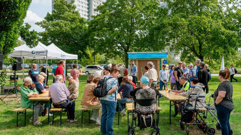 Informations- und Beteiligungsveranstaltung von degewo im Wohnquartier Marzahn mit Dialogstation und zahlreichen Anwohnenden vor einem Hochhaus.