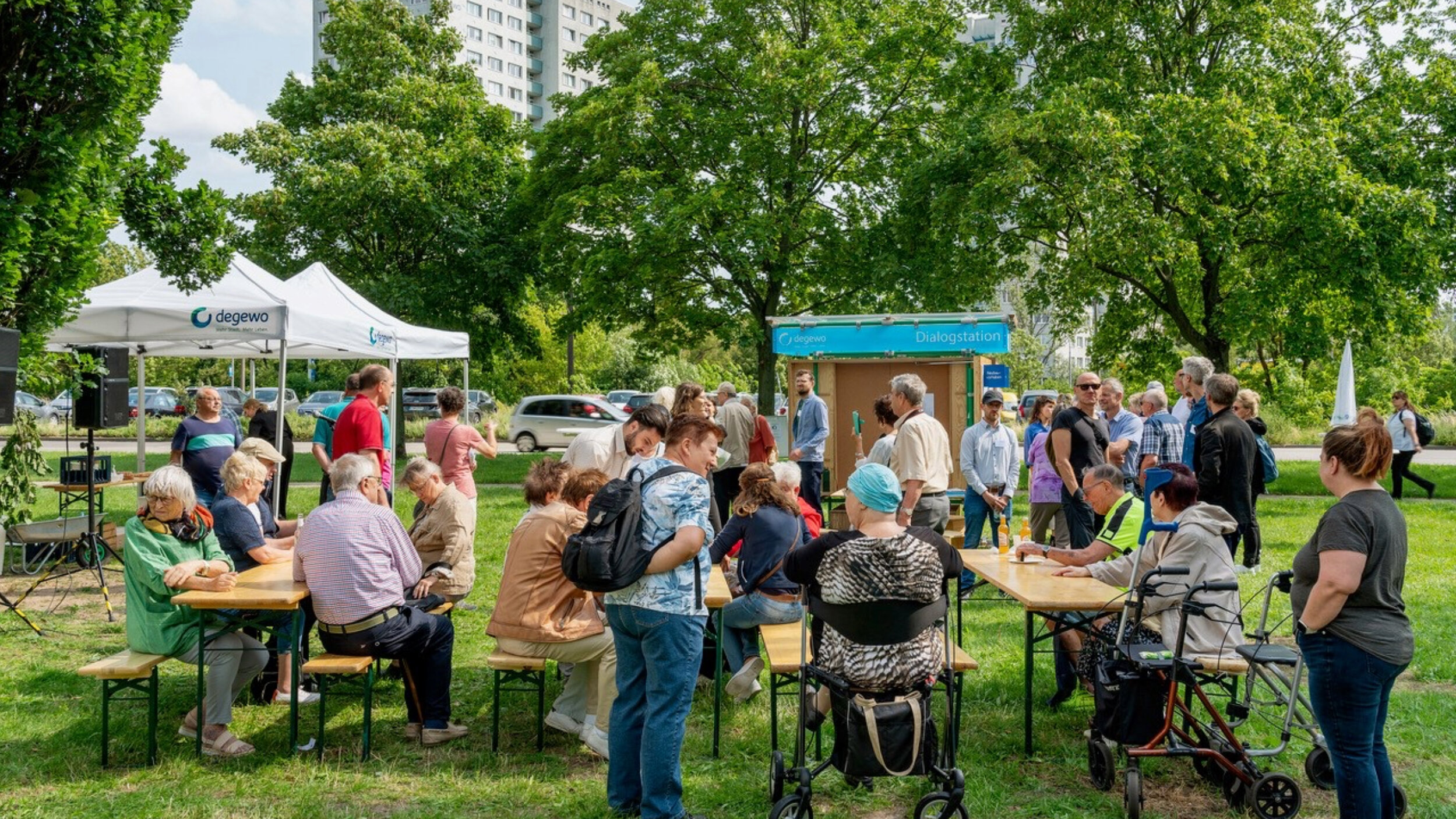 Informations- und Beteiligungsveranstaltung von degewo im Wohnquartier Marzahn mit Dialogstation und zahlreichen Anwohnenden vor einem Hochhaus.