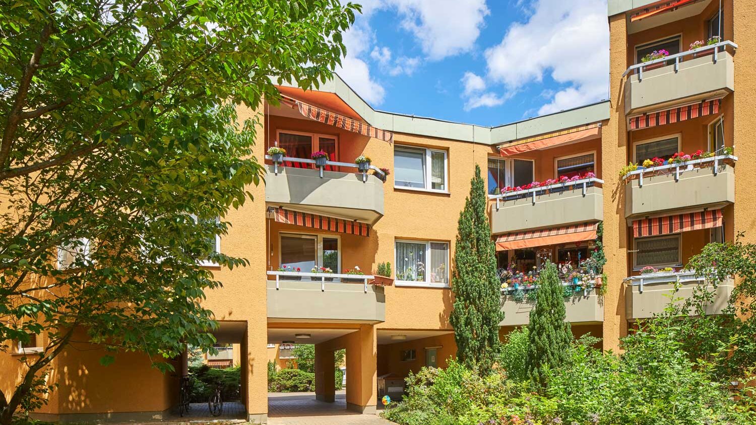 Mehrgeschossige Wohnhäuser der Horstwalder Straße mit Balkonen und üppiger Bepflanzung. Sonnige Grünanlage im Vordergrund.