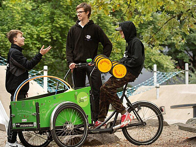 Mann und Jungs unterhalten sich, Junge sitzt auf Lastenrad.