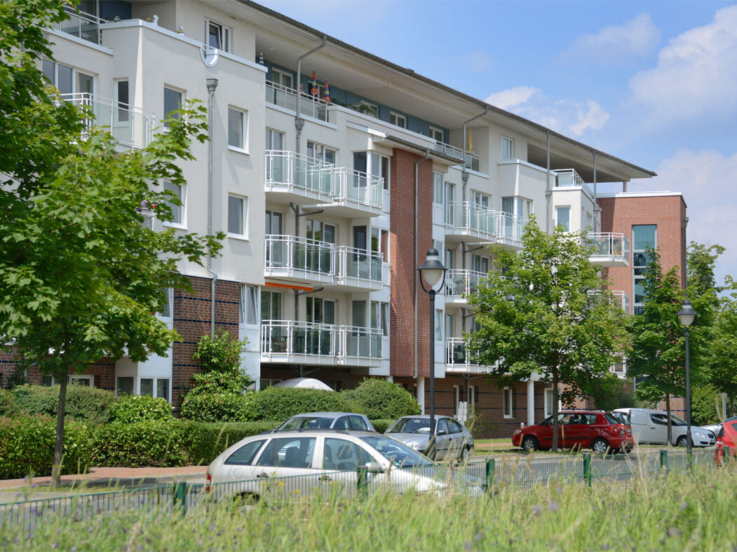 Ein großes Wohnhaus mit Klinkerfassade, Balkonen und viel Grün davor.
