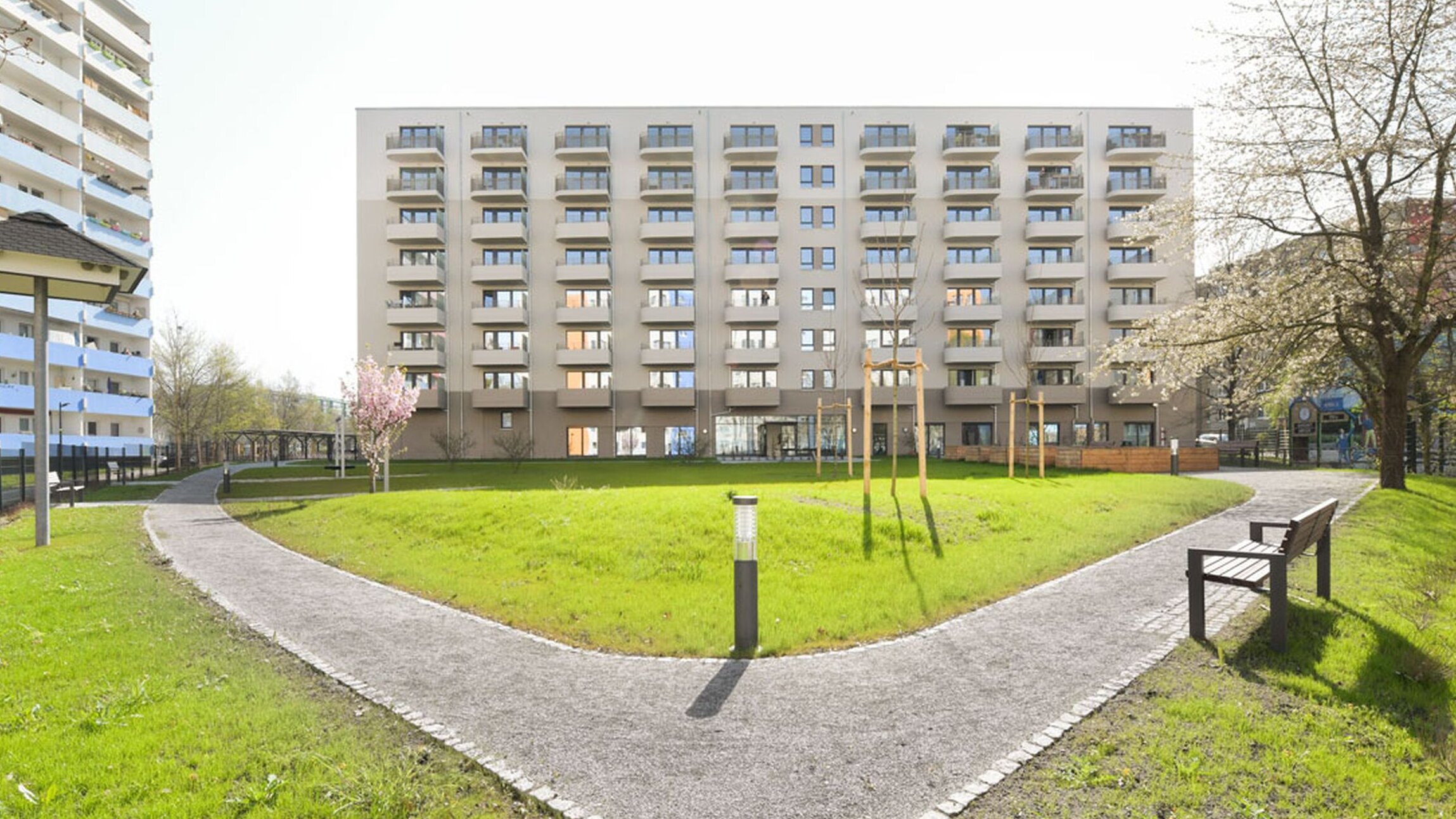 Außenansicht degewo-Neubau Venusstraße 28 mit Grünflächen, Weg, Weglaterne und Bank im Vordergrund.