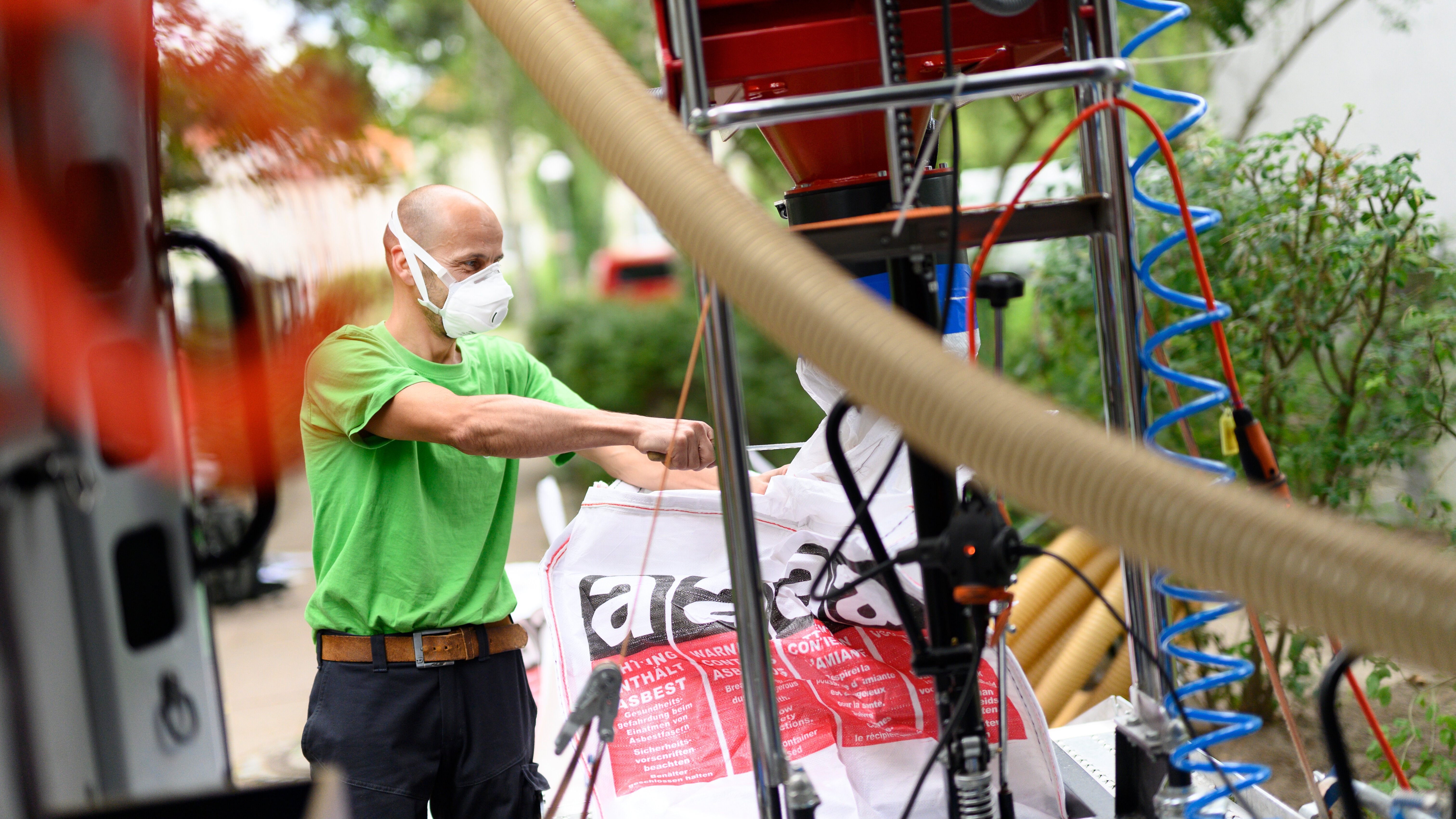 Mann mit Schutzmaske füllt Sack an technischer Anlage.