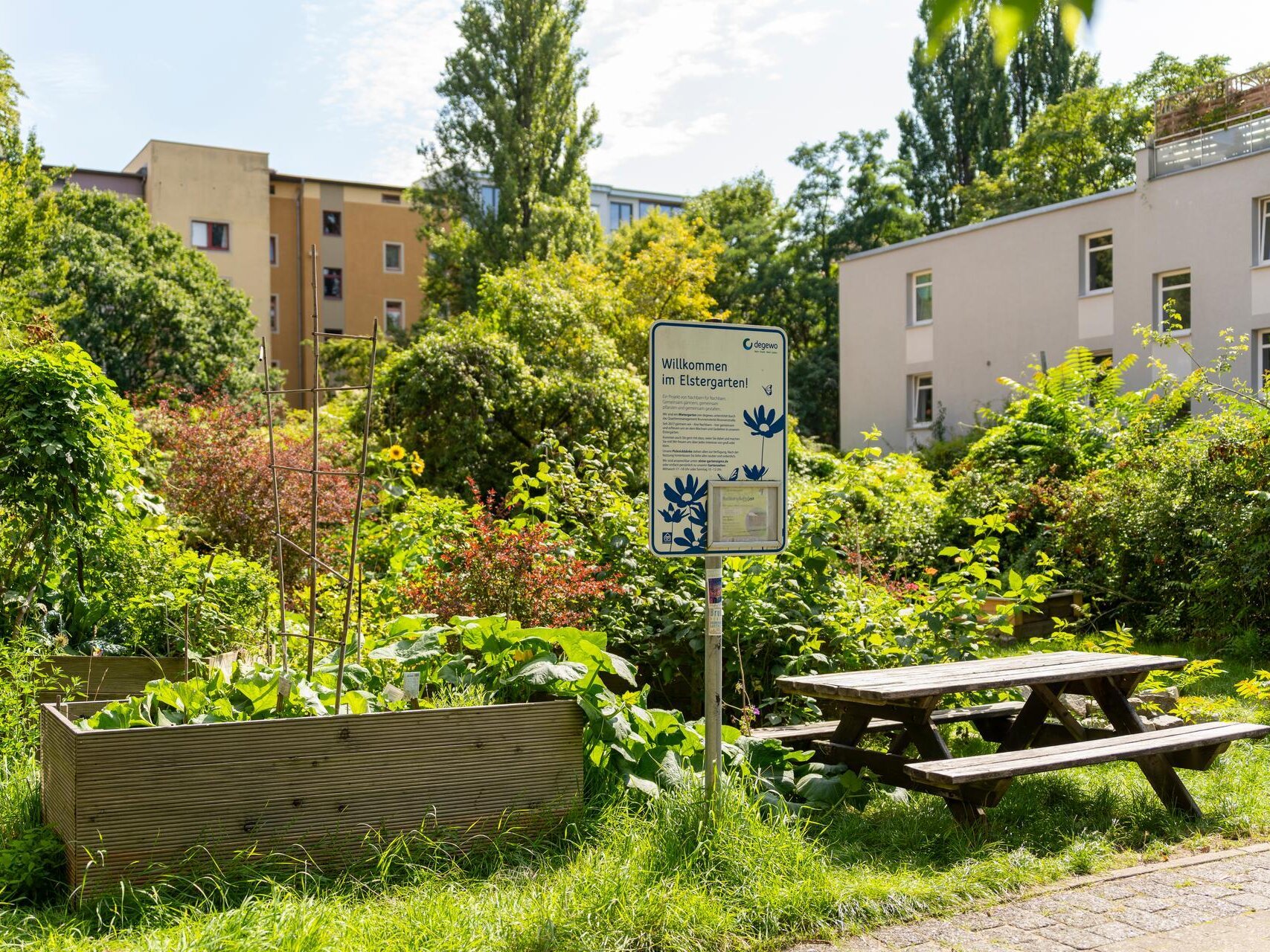 Ein grüner Garten inmitten eines Wohnkomplexes. In der Mitte steht ein Schild mit dem Namen Elstergarten.