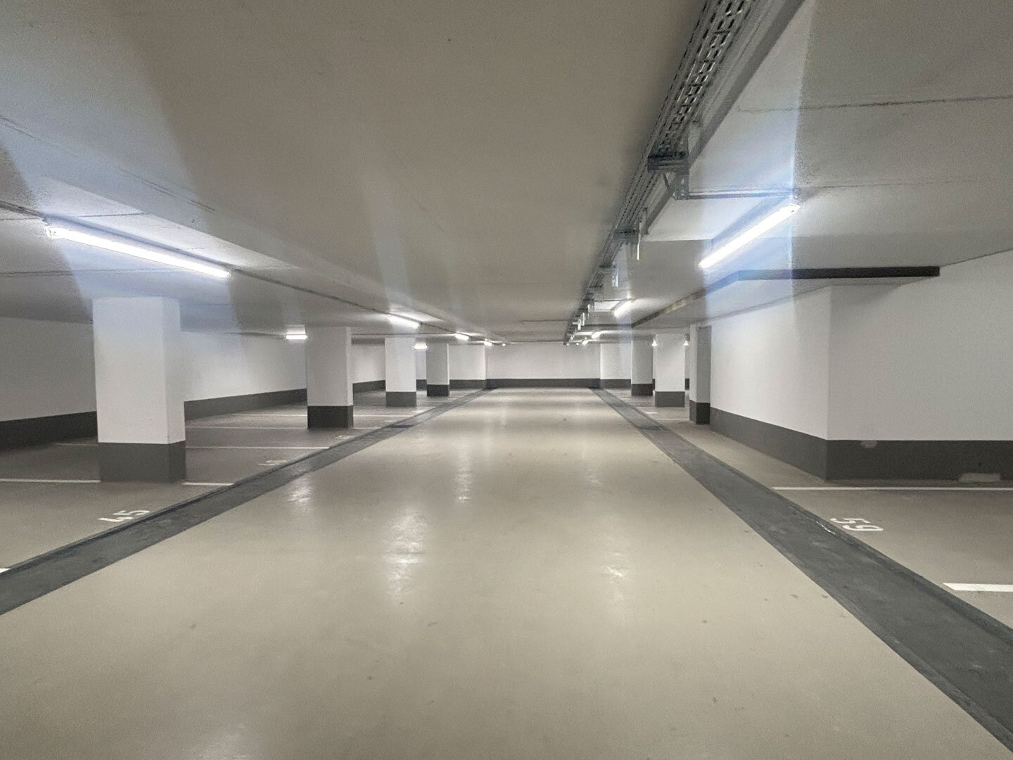 Innenansicht einer Tiefgarage. Sie ist leer, die Lichter sind an.