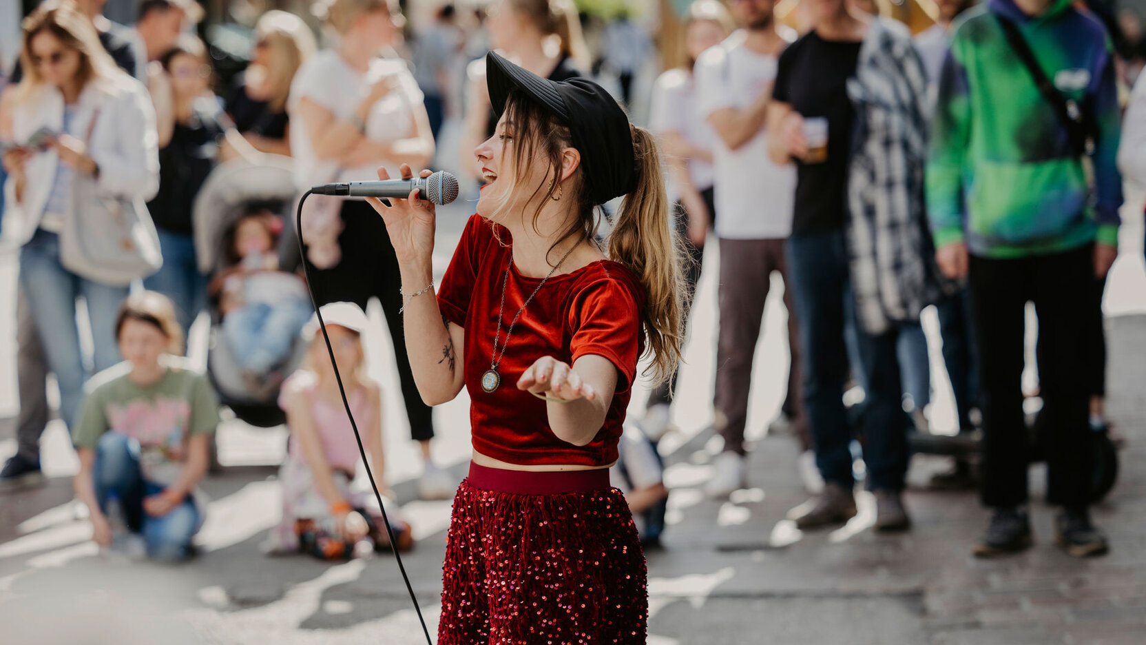 Eine Musikerin steht auf der Straße, trägt ein rotes Kleid und singt vor Publikum.