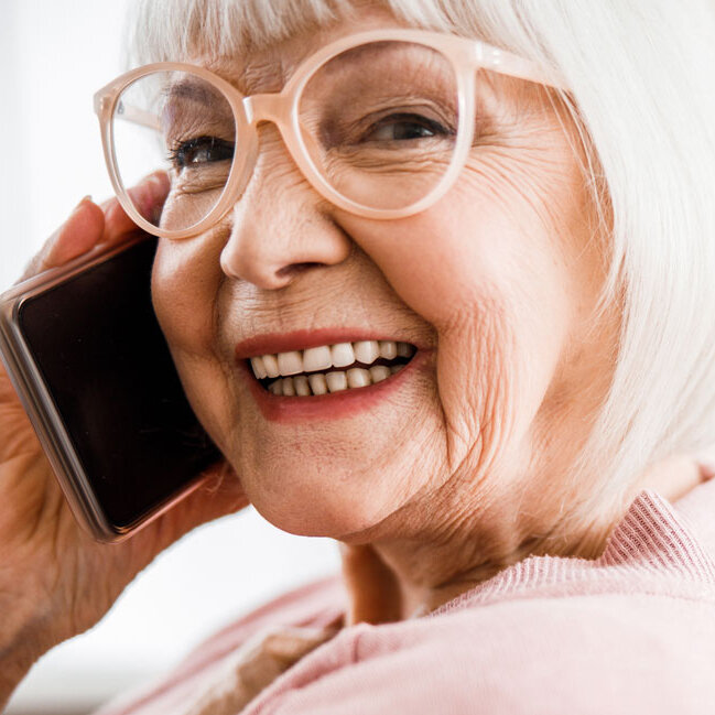 Eine ältere Frau lächelt in die Kamera während sie telefoniert. 