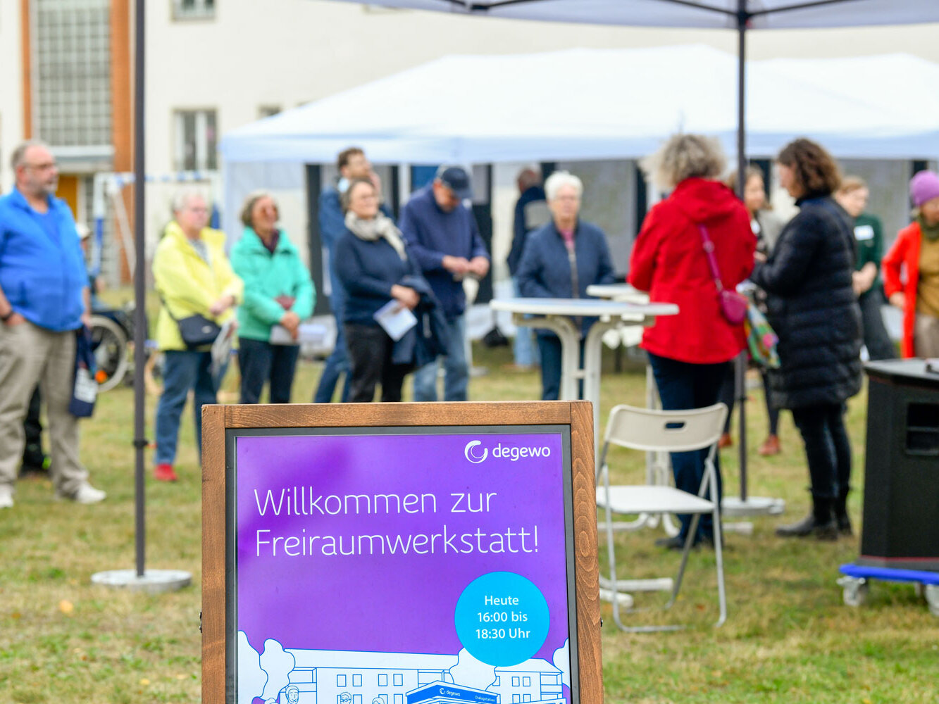 Aufsteller mit der Aufschrift "Willkommen zur Freiraumwerkstatt!", im Hintergrund mehrere Personen auf einem Platz