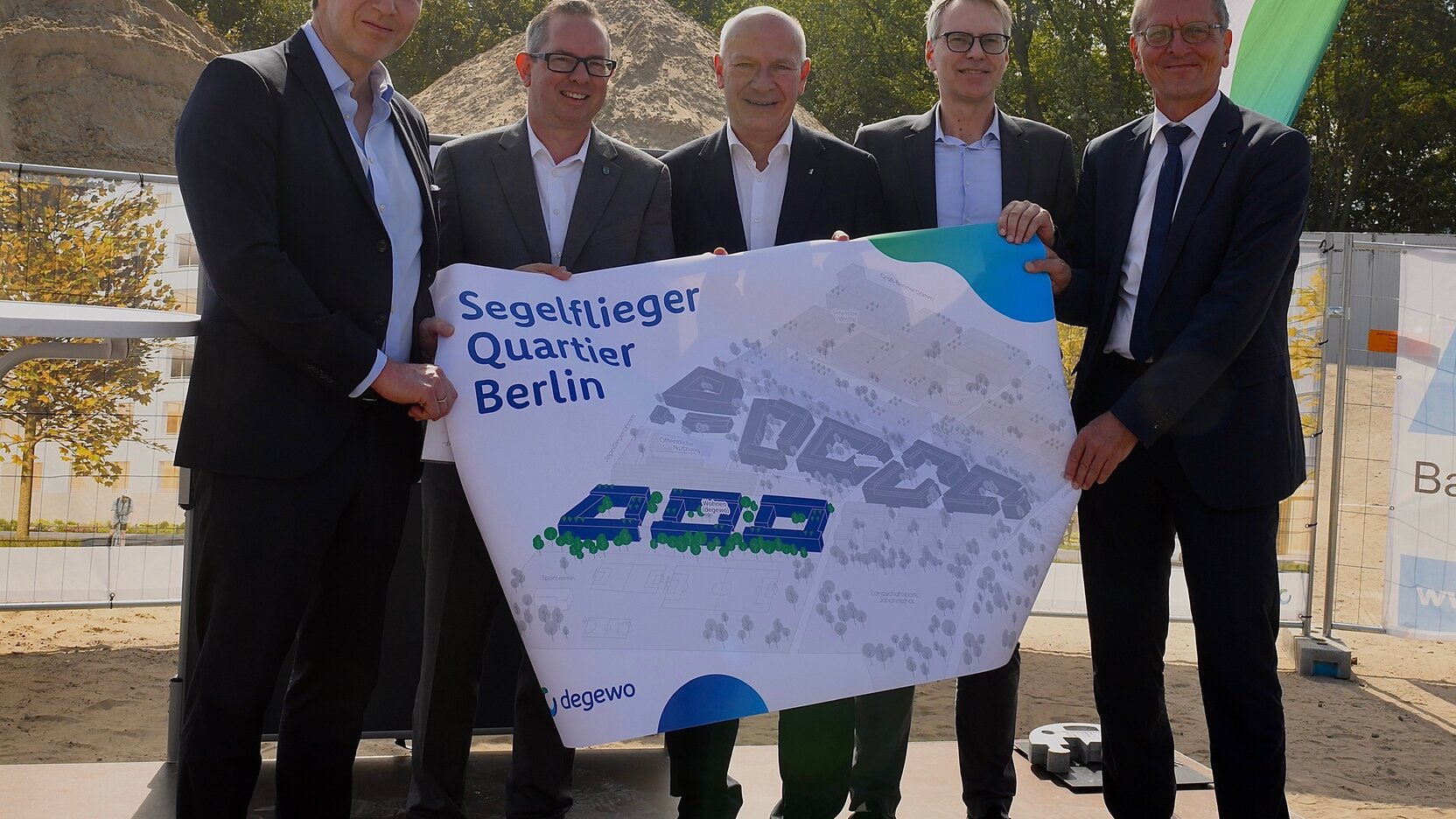 v.l.n.r.: Daniel Herrmann, Vorstand der BAUWERT AG; Oliver Igel, Bezirksbürgermeister von Berlin Treptow-Köpenick; Kai Wegner, Regierender Bürgermeister von Berlin; Kai-Marten Maack, Vorstandsmitglied degewo; Christian Gaebler, Senator für Stadtentwicklung, Bauen und Wohnen beim Projektstart am Segelflieger Quartier mit einem Plan des Quartiers