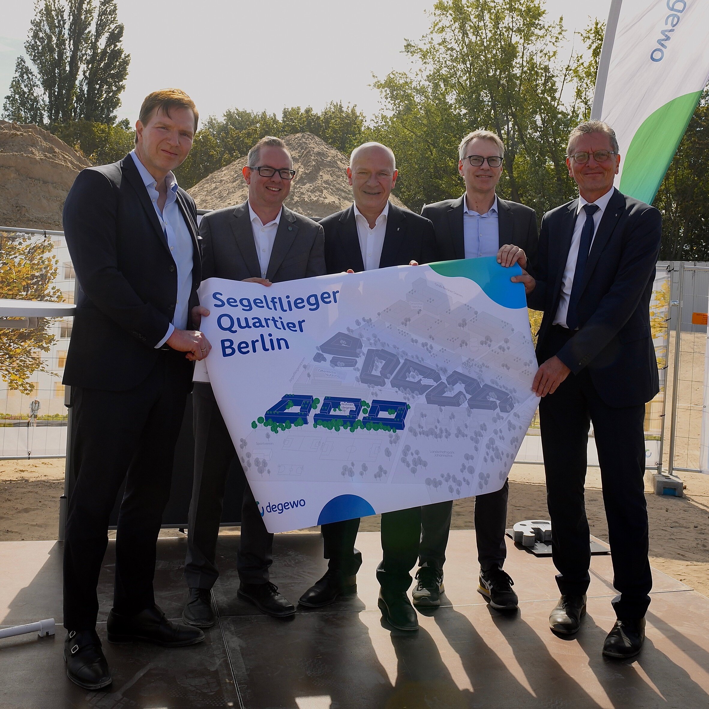 v.l.n.r.: Daniel Herrmann, Vorstand der BAUWERT AG; Oliver Igel, Bezirksbürgermeister von Berlin Treptow-Köpenick; Kai Wegner, Regierender Bürgermeister von Berlin; Kai-Marten Maack, Vorstandsmitglied degewo; Christian Gaebler, Senator für Stadtentwicklung, Bauen und Wohnen beim Projektstart am Segelflieger Quartier mit einem Plan des Quartiers