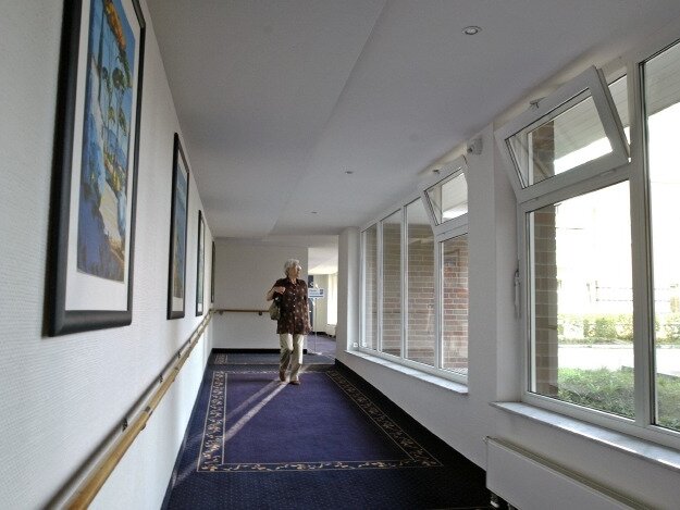 Seniorin läuft auf dem langen Flur mit vielen Fenstern 