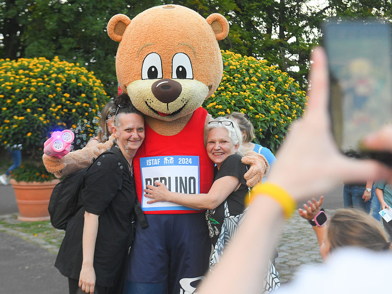 Ein großes Bären-Maskottchen posiert für eine Foto mit den Besuchern eines Parks.