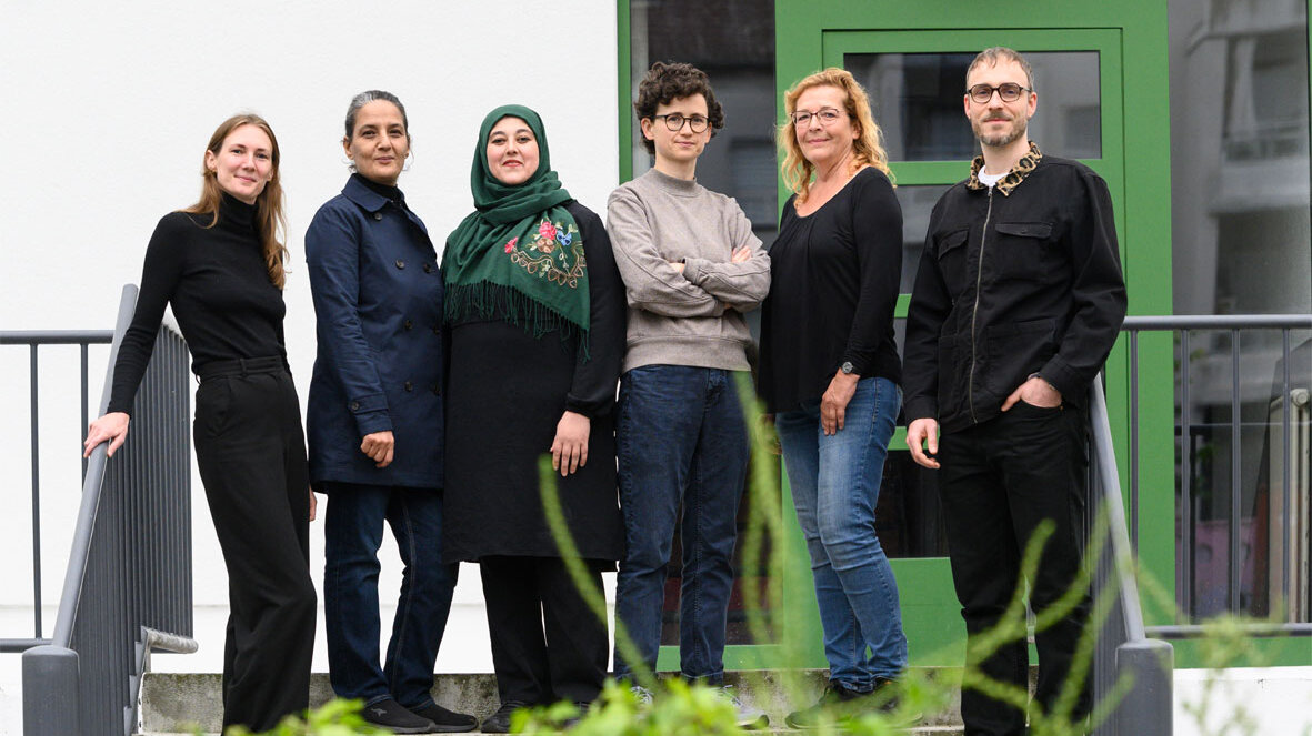 Gruppenaufnahme des Mieterbeirates Mariannenplatz: Sechs Menschen stehen im Freien auf einer Treppe vor einer grünen Tür.